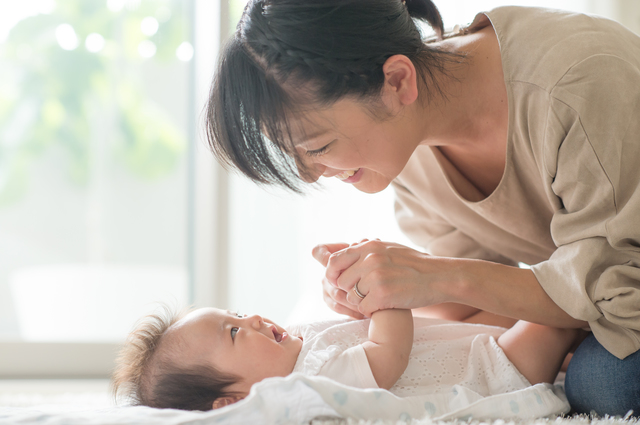 女性に手を握られて笑顔の赤ちゃん