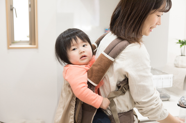 おんぶ紐で赤ちゃんをおんぶしながら家事をする女性