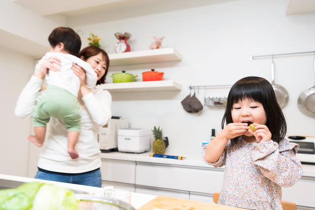 息子を抱っこする母親とキッチンでつまみ食いする女の子